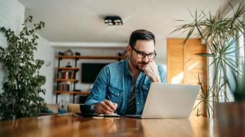 a man sitting at a table looking at his laptop