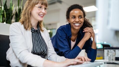 two women sitting at a table with a laptop
