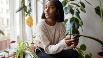 a woman sitting on a window sill holding a cell phone