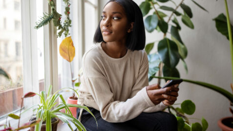 a woman sitting on a window sill holding a cell phone