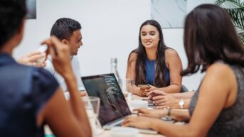 a group of people sitting around a table with laptops