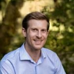 a man in a blue shirt smiling for the camera