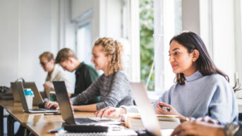a group of people sitting at a table with laptops