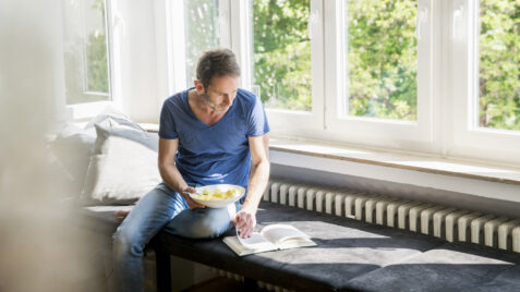 a man sitting on a bench eating cereal and reading a book