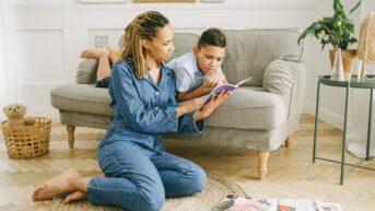 a woman sitting on the floor reading a book to a boy
