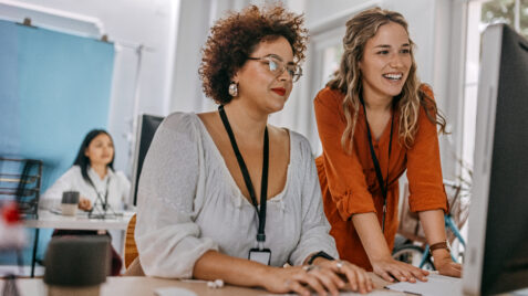 two women sitting at a table with a laptop