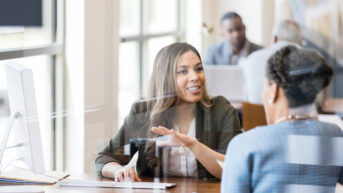 a woman talking to another woman at a desk