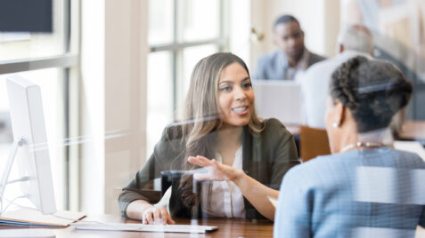 a woman talking to another woman at a desk