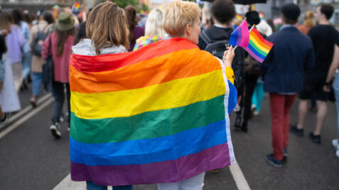 a group of people walking down a street holding a rainbow flag for Pride Month