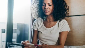 a woman sitting on a bed looking at her cell phone