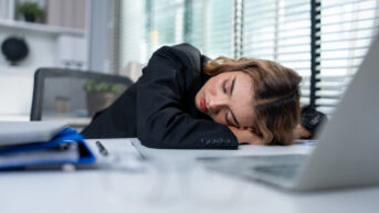 a woman sleeping on a desk in front of a laptop