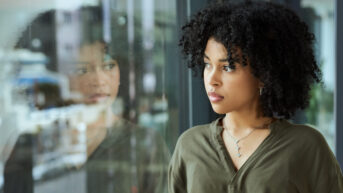 A woman at work feeling stressed about uncertainty and staring out the window.