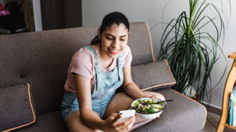 woman sitting on couch with healthy meal and digital mental health app