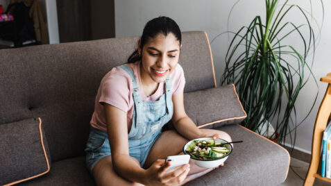 woman sitting on couch with healthy meal and digital mental health app