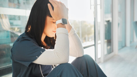 a healthcare worker sitting on the floor with her head in her hands
