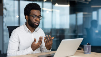 a man sitting at a desk in front of a laptop, speaking to EAP counselor