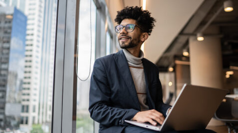 a man in a suit sitting on a window sill using a laptop