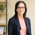 a woman wearing glasses standing in front of a desk