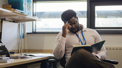 a man sitting at a desk talking on a cell phone