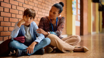 a woman sitting next to a boy on the floor